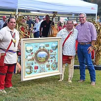 A group of guests, some in traditional regalia, holding a framed artwork at an outdoor fall gathering